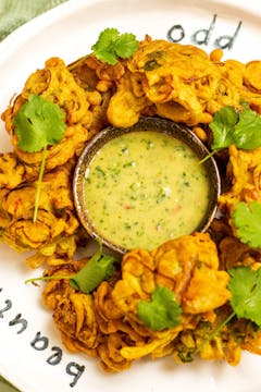 A plate of crispy leek pakoras surrounding a bowl of coconut herb chutney.