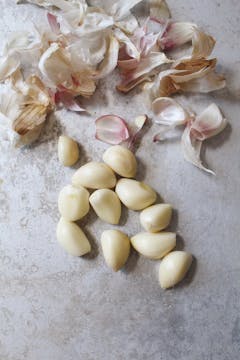 11 peeled cloves of garlic on a countertop. There's a pile of peels above them.