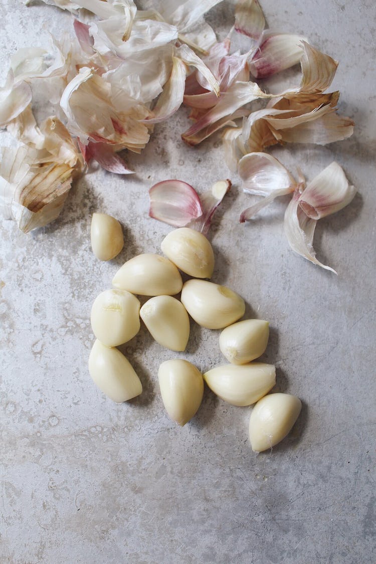 11 peeled cloves of garlic on a countertop. There's a pile of peels above them. 