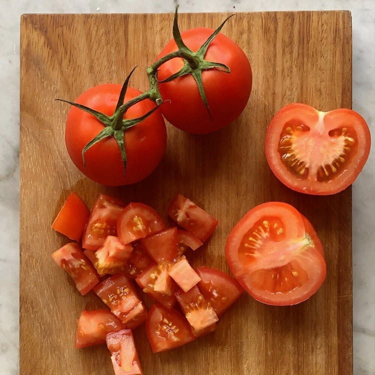 Tomatoes on a chopping board. There are two whole ones, one cut into two halves, and a pile of chopped tomatoes.