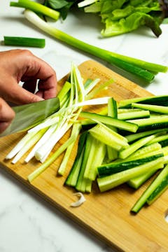 Cucumber and spring onion being sliced into thin matchsticks, each around 10cm long. 
