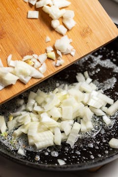 diced onion being added to a buttery pan 