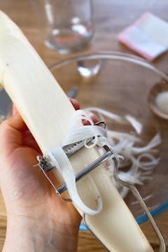 mooli radish being julienned with a peeler