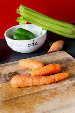 carrots on a wooden chopping board with celery and pepper in the background