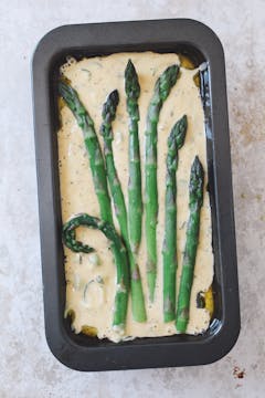A pan of raw batter about to be put into the oven. The top is decorated with 7 whole asparagus spears.