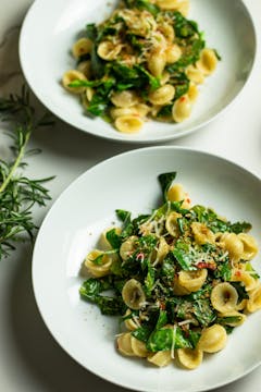two plates of pasta with spring greens