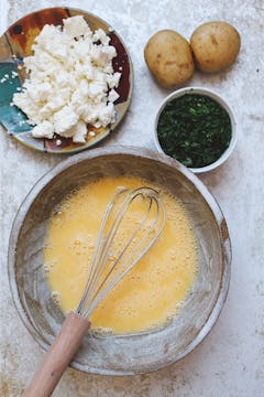 A bowl of whisked eggs, with a bowl of feta and a bowl of chopped parsley next to it. 