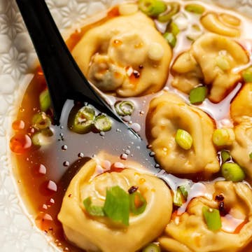 Celery and kale wonton soup with a black spoon