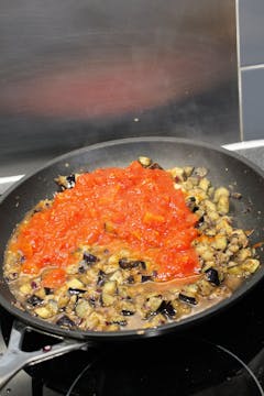  In a saucepan, red onion, aubergine and tin chopped tomato in the process of cooking
