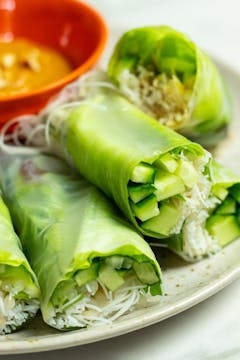 A plate with 5 Vietnamese summer rolls. A bowl of peanut dipping sauce is visible in the background. 