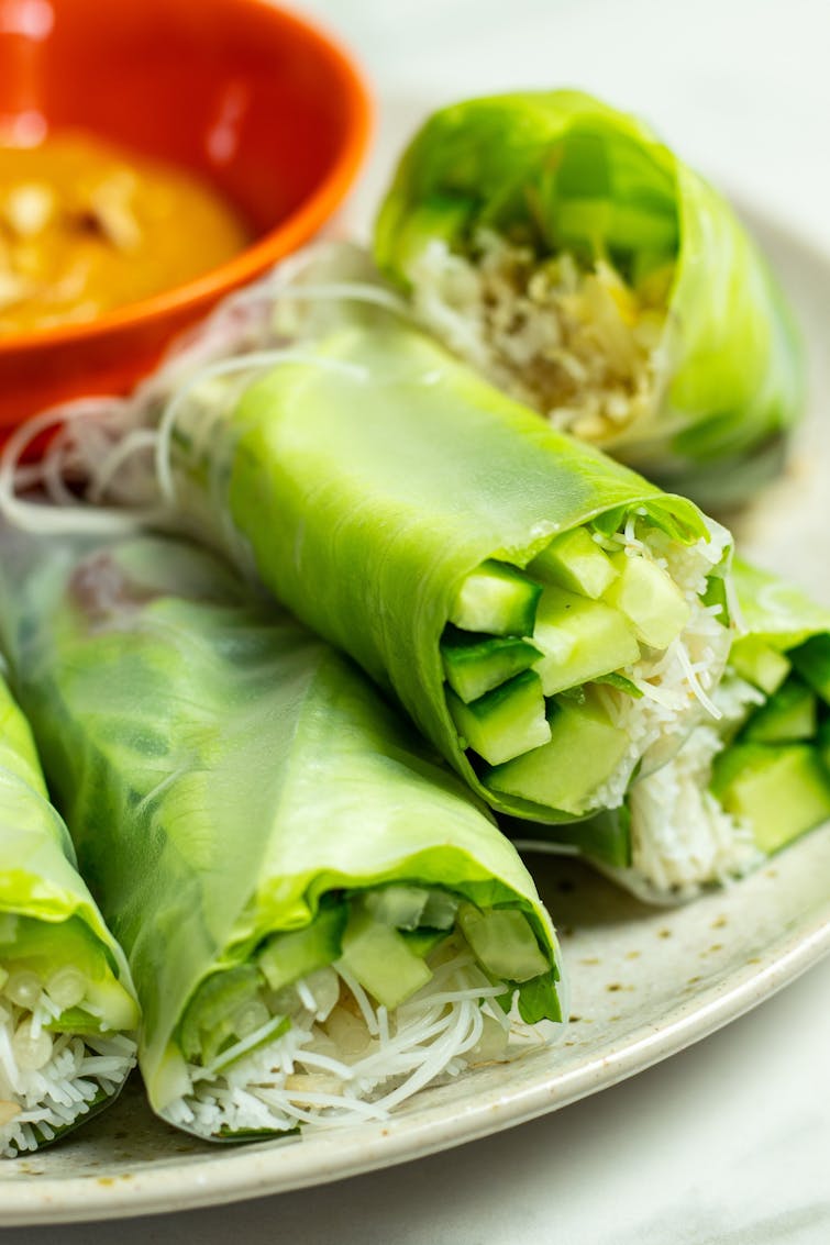 A plate with 5 Vietnamese summer rolls. A bowl of peanut dipping sauce is visible in the background.