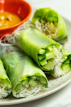 A plate with 5 Vietnamese summer rolls. A bowl of peanut dipping sauce is visible in the background. 