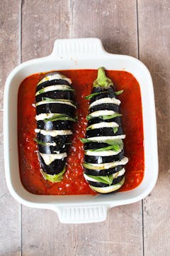 stuffed aubergine in baking dish with tomato sauce ready for baking