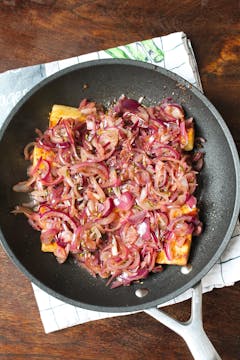 red onions on top of parsnips in a frying pan