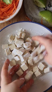 cubes of tofu being tossed in cornflour 