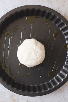 The ball of pizza dough sitting on a greased baking tray. 