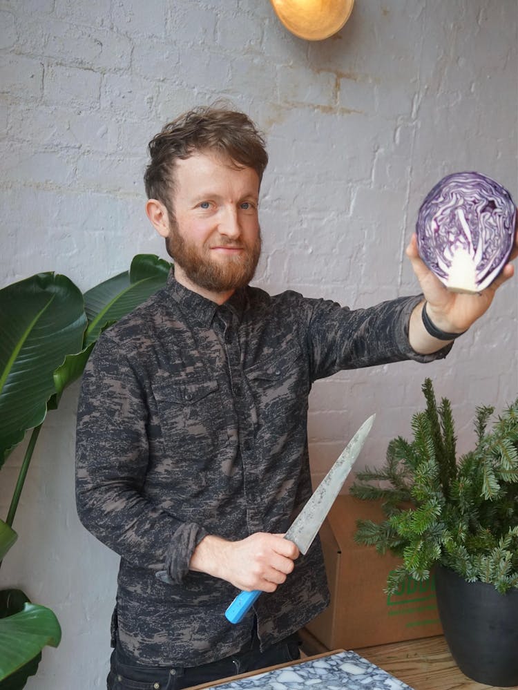 Douglas McMaster holding a purple cabbage and a knife, about to prep it. 