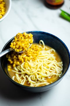 The ramen bowl being built, with corn being put on top of the noodles in the broth.