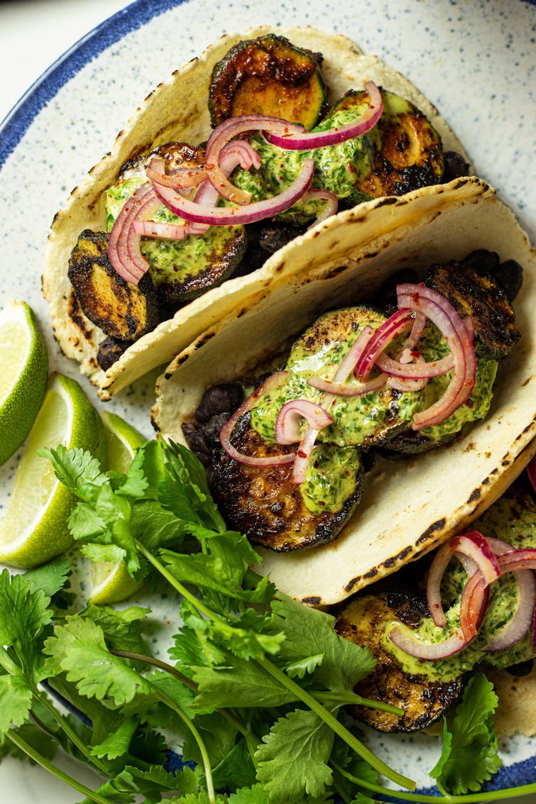 two soft shell taco filled with smokey courgette garnished with red onion and drizzled with mayo
