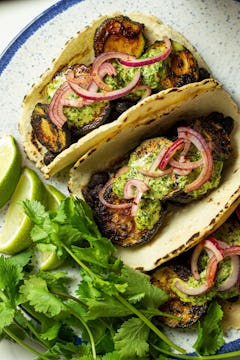 two soft shell taco filled with smokey courgette garnished with red onion and drizzled with mayo
