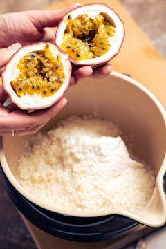 in a large bowl wet and dry ingredients for the cheesecake and hand holding whole passionfruit cut into half