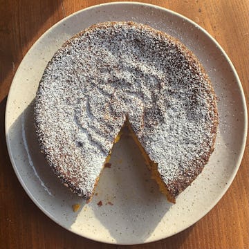 whole Orange & Almond Cake with a slice missing dusted with icing sugar
