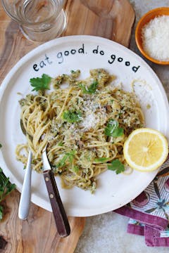 served fennel pasta garnished with herbs on plate along with cutlery and half a lemon
