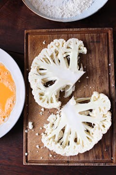 cauliflower slices on a wooden chopping board