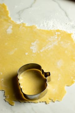 Dough rolled out flat and being cut with a pumpkin-shaped cutter.