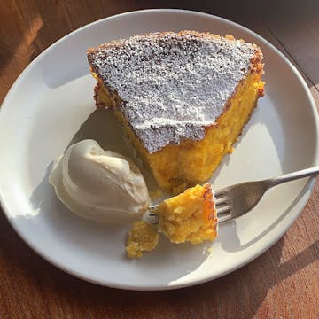 piece of Orange & Almond Cake dusted with icing sugar, a little piece cake from the slice is on the fork , served with scope of vanilla ice cream.