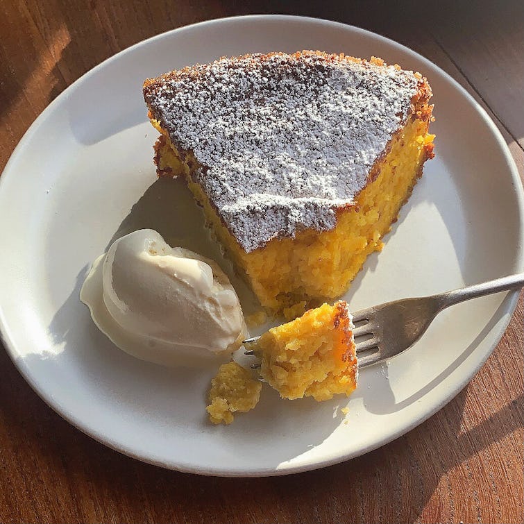 piece of Orange & Almond Cake dusted with icing sugar, a little piece cake from the slice is on the fork , served with scope of vanilla ice cream.