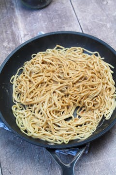 Cooked noodles in a pan mixed in with some peanut sauce. 