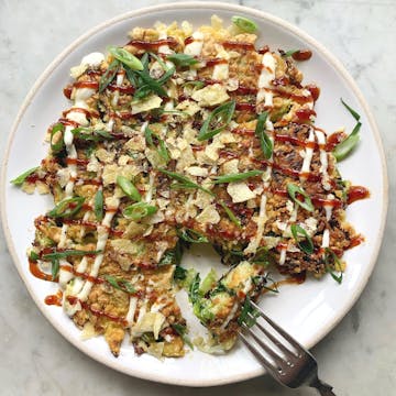 plate of finished savoy cabbage Okonomiyaki garnished with mayonnaise, spring onion tops and crisps