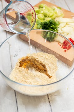Water being added to a mixing bowl of gran flour, plain flour, and the spices in this recipe. 