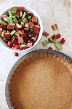 Brown sugar spread evenly on a pie tin, forming a crust. There is a bowl of rhubarb left of the tin.