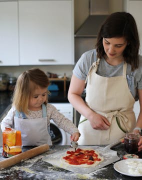 little girl and mum putting sauce on a homemade pizza