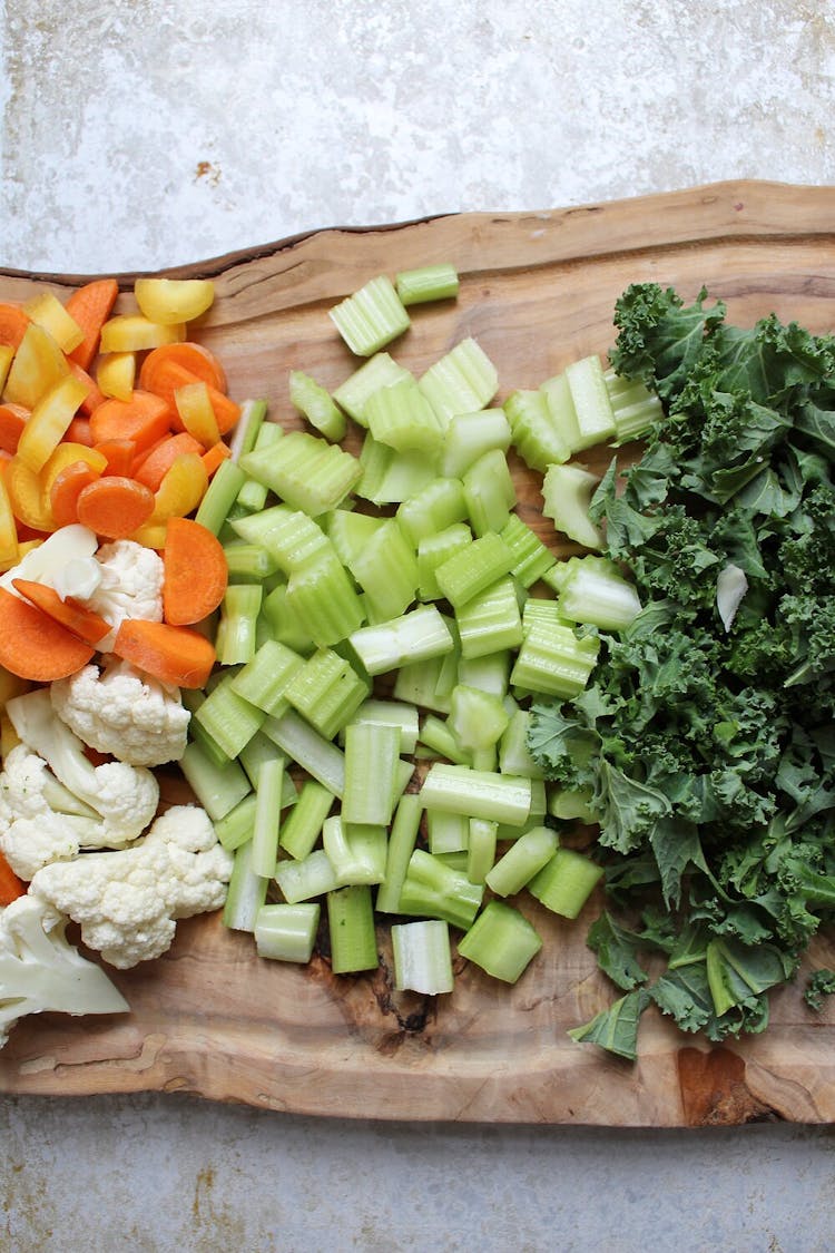 Chopped celery on a chopping board with carrots, cauliflower, and kale.