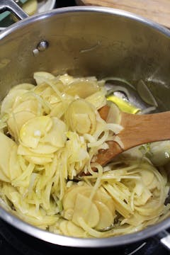 Finely sliced potatoes and onions frying in a pot. 