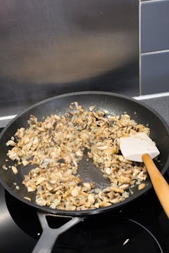 Onion, ginger, mushrooms, and garlic being fried in a pan. 
