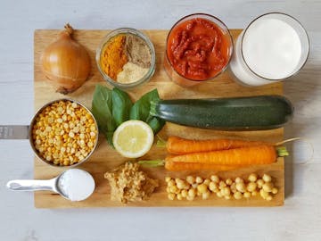 The ingredients needed for a mild peanut and coconut milk curry. Onion, spices, tomato puree, coconut milk, moong daal, lemon, basil, courgette, carrot, chickpeas, peanut butter, and cornflour.