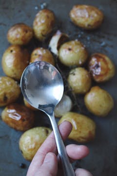 roasted potatoes in the background and spoon being help upclose