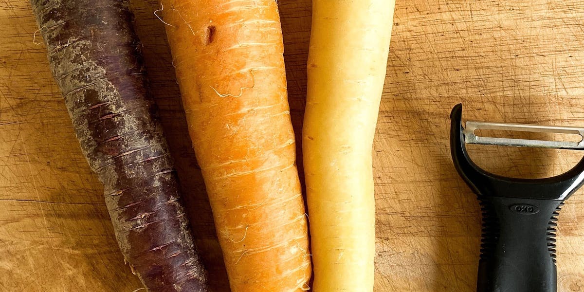3 rainbow coloured carrots and parsnips and a peeler