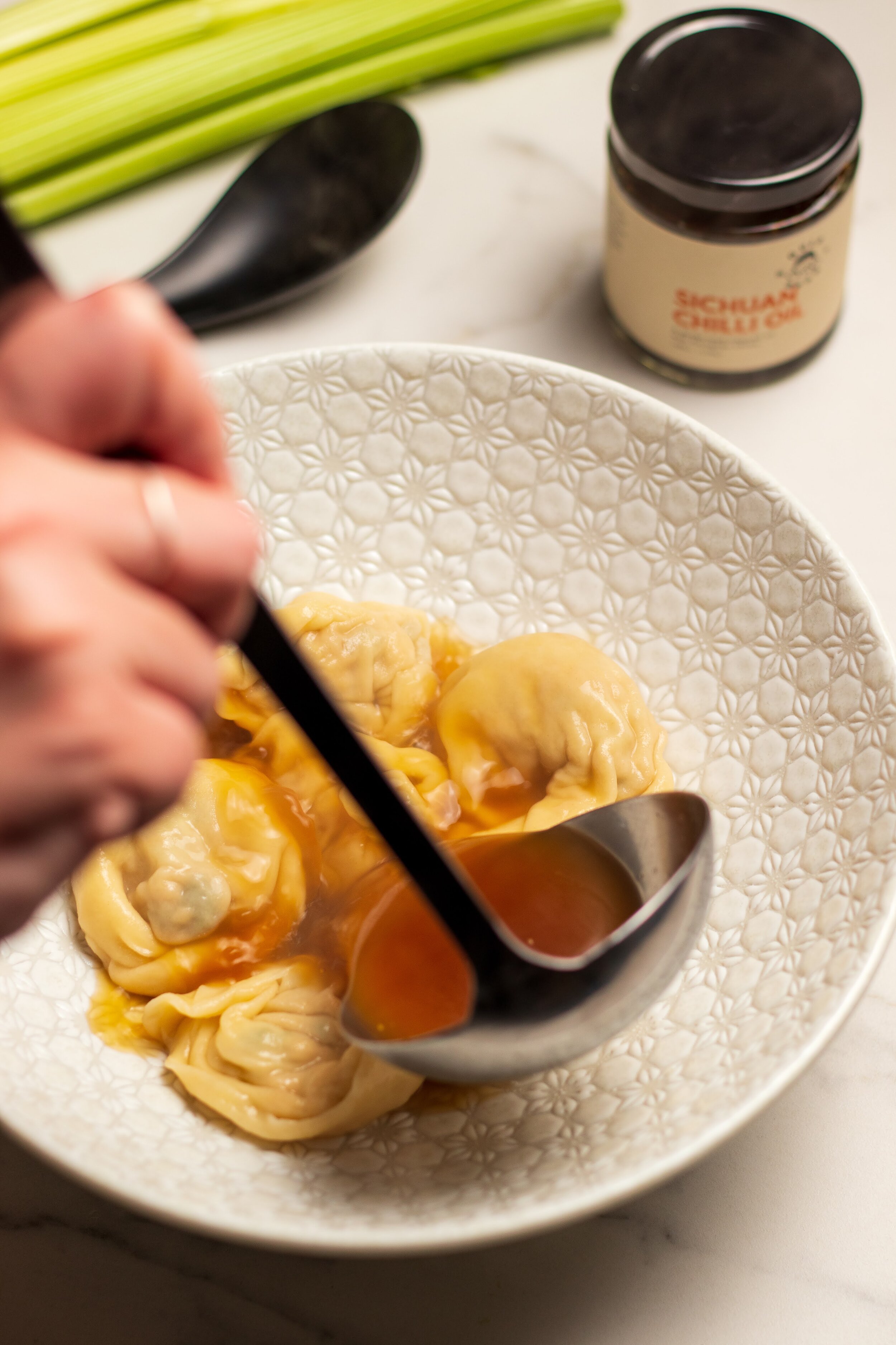 about 7 or 8 wonton dumplings added to a dish and broth is being poured over 