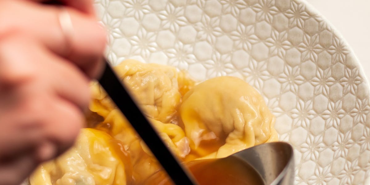 about 7 or 8 wonton dumplings added to a dish and broth is being poured over