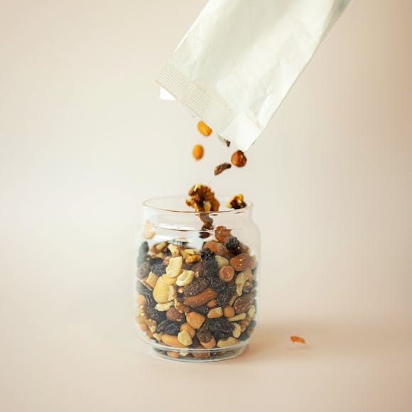 Glass jar being filled with fruit and nut mix.