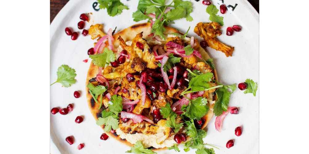 Cauliflower pittas topped with coriander and pomegranate seeds on a white plate