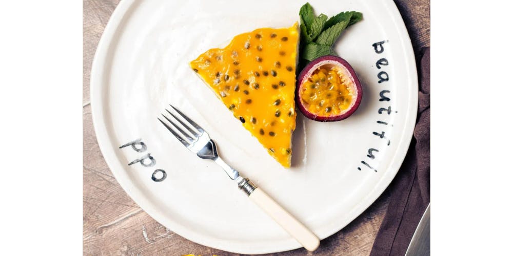 Vegan passionfruit cheesecake on a white plate with half of a passionfruit next to it 