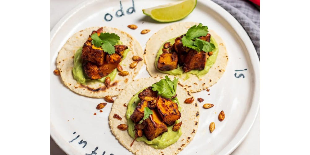 Butternut squash tacos on a white plate with a lime wedge 