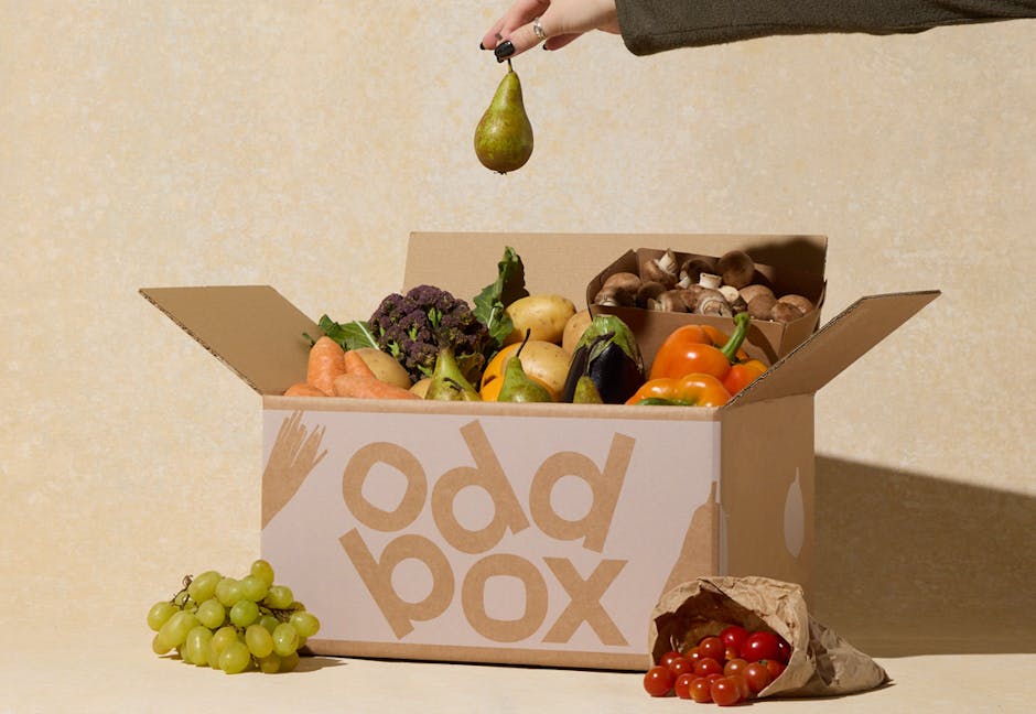 Oddbox filled with fruit and veg and a hand holding a pear.