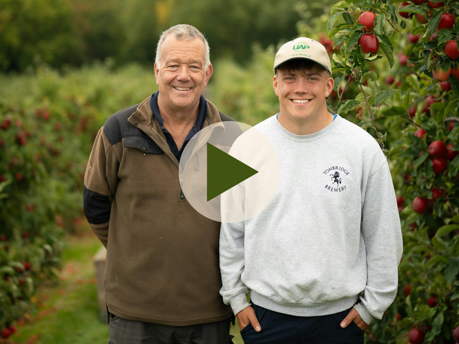 Northiam Farm Growers - father and son smiling to camera with video play button overlaid.